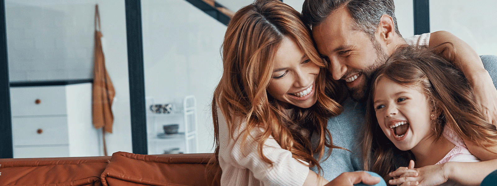 family of young parents and young daughter snuggling together at home.